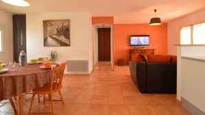A dining area with a table set for four, a sofa, a television, and a door leading to another room. - Holiday Home in Avrille Near Sandy Beaches (Avrille)