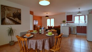 A dining area with a round table, chairs, a painting on the wall, a potted plant, and a kitchen in the background. - Holiday Home in Avrille Near Sandy Beaches (Avrille)