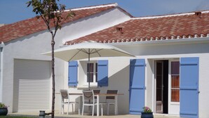 A building with a tiled roof, a covered patio with a table and chairs, and a garage door. - Holiday Home in Avrille Near Sandy Beaches (Avrille)
