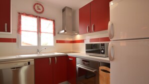 A kitchen with red cabinets, a Bosch dishwasher, a microwave, an oven, and a refrigerator. - Holiday Home in Avrille Near Sandy Beaches (Avrille)