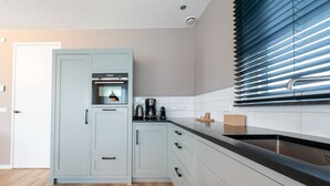 A modern kitchen with light blue cabinets, a black countertop, and a built-in oven. - Holiday Home in Texel Near the Sea (De Koog)