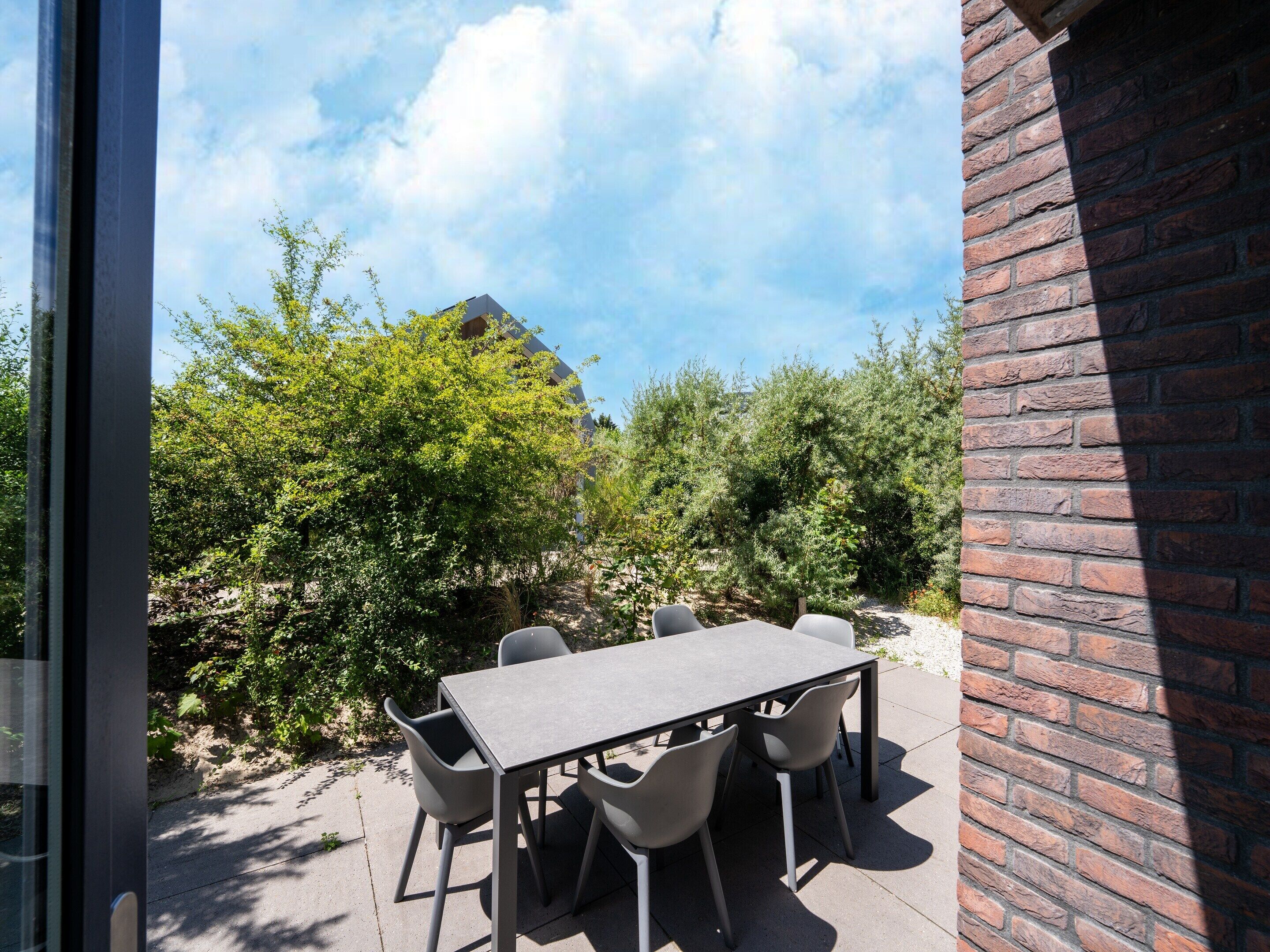 Une terrasse extérieure avec une table et des chaises, entourée de verdure et d’un mur de briques.
