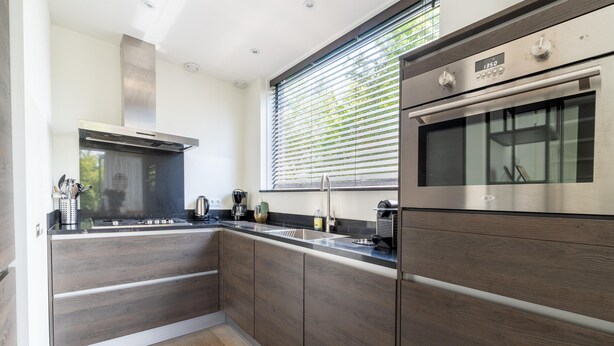 Una cocina moderna con armarios de madera oscura, electrodomésticos de acero inoxidable y un ventanal con persianas.