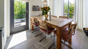 Un comedor con una mesa de madera, cuatro sillas, un florero con girasoles y una lámpara colgante.