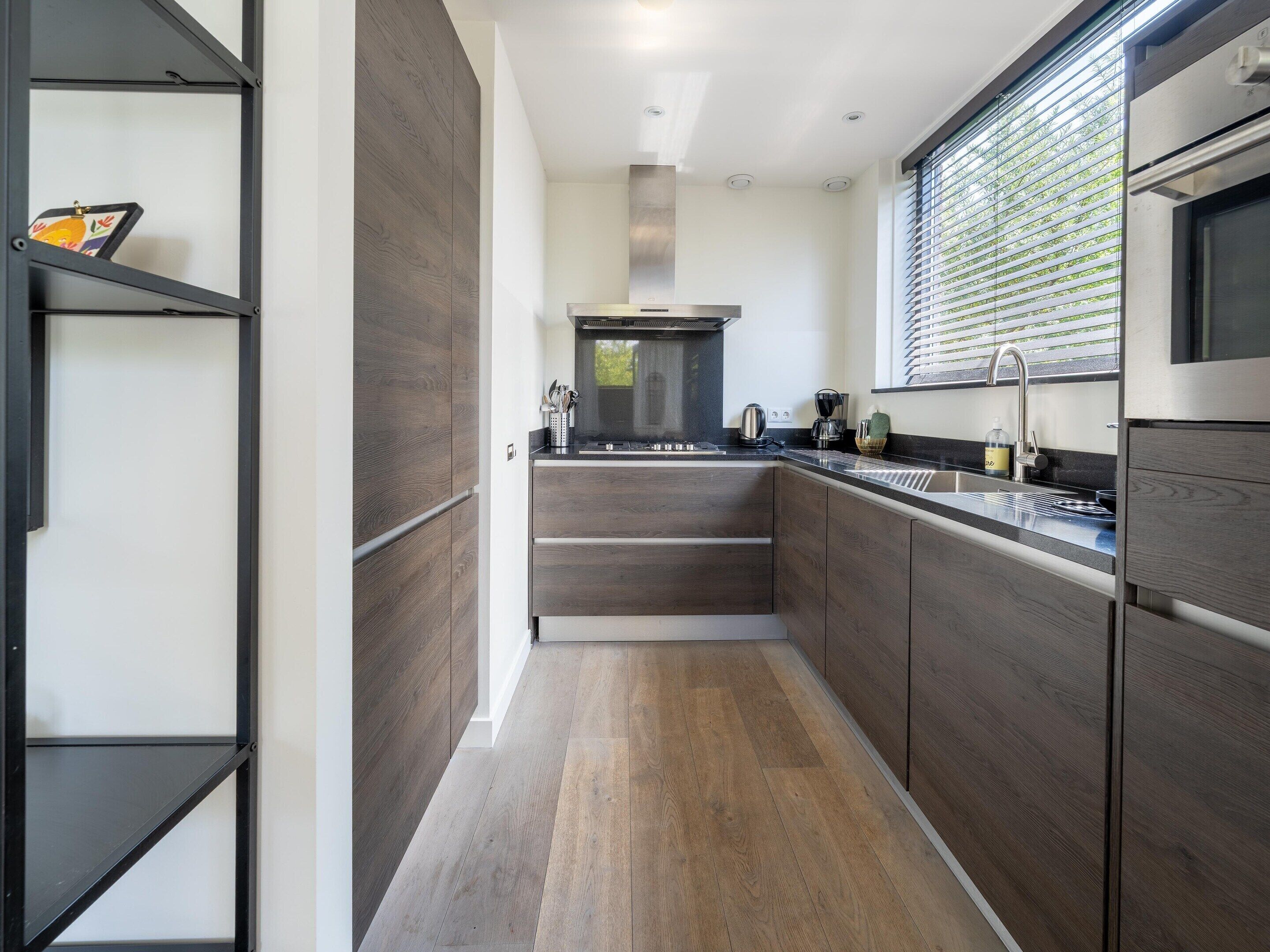 A modern kitchen with dark wood cabinets, a stainless steel range hood, and a window with blinds.