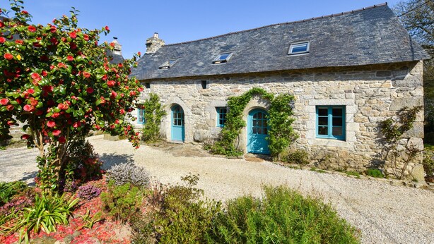 A stone house with a sloped roof, arched windows, and a gravel driveway. - 17th Century Breton Cottage With Modern Interior on the Edge of a Forest (Huelgoat)