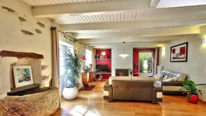 A living room with a sofa, a coffee table, a fireplace, and a large potted plant. - 17th Century Breton Cottage With Modern Interior on the Edge of a Forest (Huelgoat)