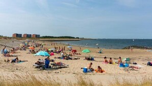 A beach with people sunbathing and swimming, umbrellas, and buildings in the background. - Lovely Cottage near Sea in Wemeldinge (Wemeldinge)