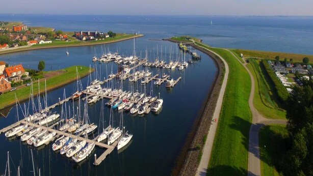 A marina with numerous boats docked, a clear sky, and a small town in the background. - Lovely Cottage near Sea in Wemeldinge (Wemeldinge)