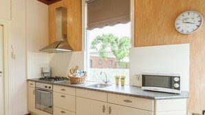 A kitchen with a stove, oven, microwave, sink, and window with blinds. - Lovely Cottage near Sea in Wemeldinge (Wemeldinge)