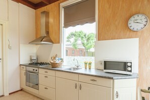 Eine Küche mit Herd, Backofen, Mikrowelle, Spüle und einem Fenster mit Jalousien.