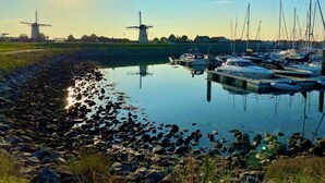 A marina with boats docked, a windmill in the background, and a calm water body reflecting the sky. - Lovely Cottage near Sea in Wemeldinge (Wemeldinge)