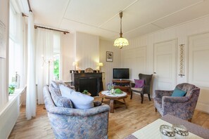 A living room with a sofa, armchairs, a fireplace, a television, and a table with decorative items.