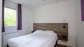 A bedroom with a wooden headboard, a white bedspread, a window with purple curtains, and a white radiator.
