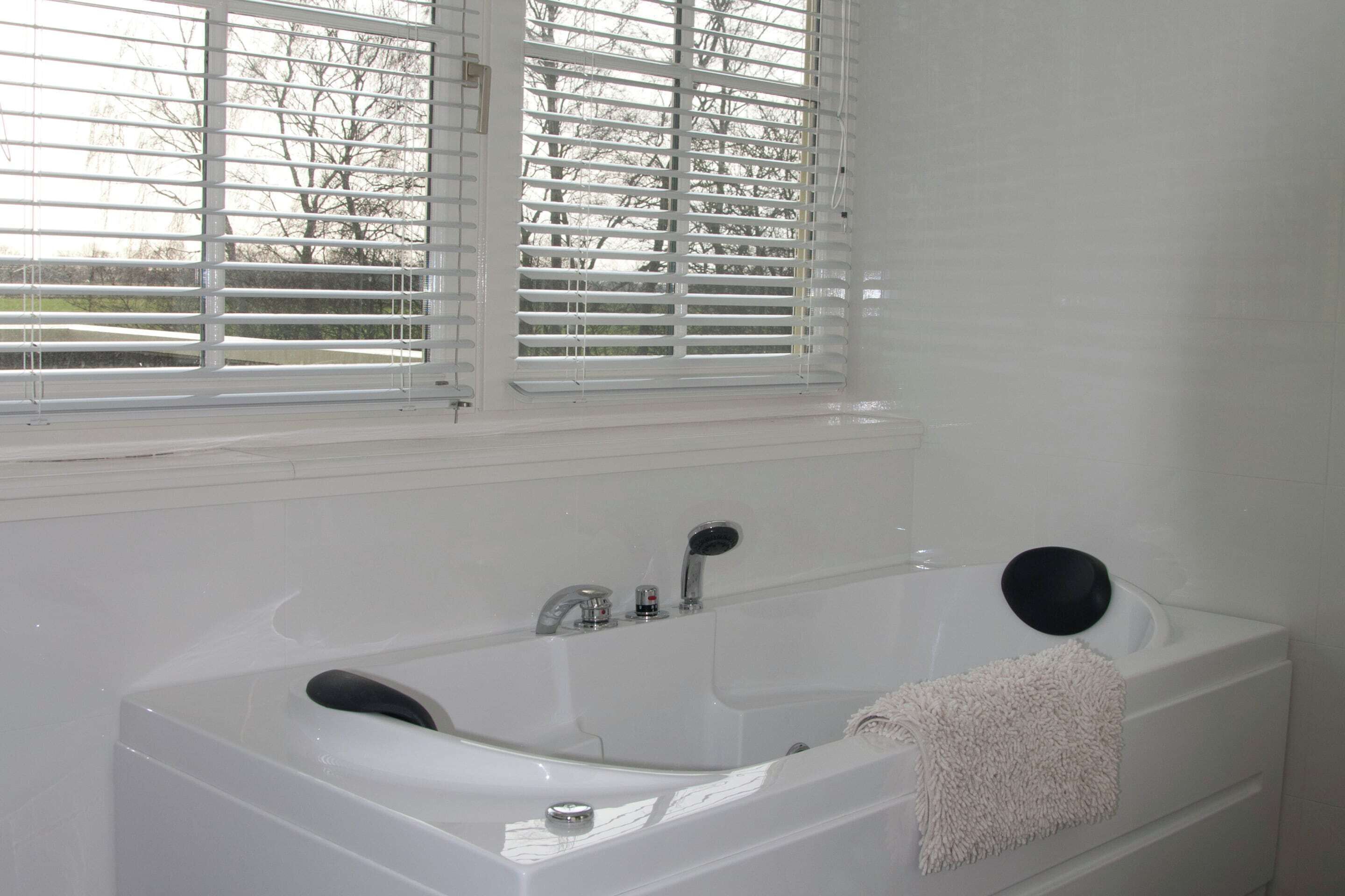 A modern bathroom with a bathtub, a window with blinds, and a towel on the side.