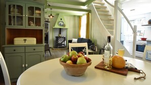 Un comedor con una mesa dispuesta para dos personas, que incluye un frutero, una botella de vino y una hogaza de pan.