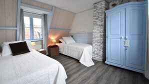 Un dormitorio con dos camas, un armario, una ventana con cortinas y una lámpara en una mesita de noche.