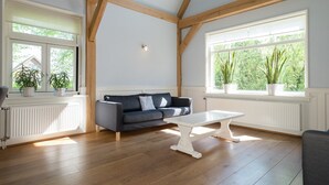 A spacious room with wooden beams, a dark blue sofa, a white table, and large windows with plants. - Inviting Holiday Home in Zuidoostbeemster near Center & Forest (Zuidoostbeemster)