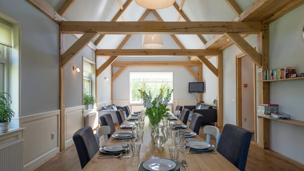 A dining area with a long wooden table set for a meal, flanked by chairs, under a high wooden beam structure with pendant lighting. - Inviting Holiday Home in Zuidoostbeemster near Center & Forest (Zuidoostbeemster)
