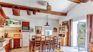 A cozy kitchen with wooden cabinets, a dining table, and chairs. There is a large window with a view of greenery outside. - Cottage in Oppede Amidst Vineyards (Oppede)