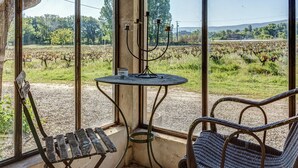 A rustic room with a large window overlooking a vineyard. There is a metal table with a candle holder and a chair. - Cottage in Oppede Amidst Vineyards (Oppede)