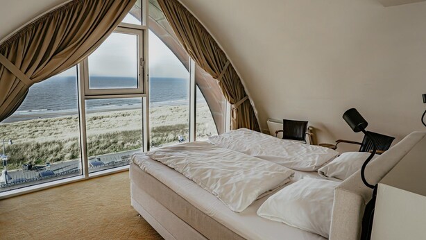 A bedroom with a large window offering a view of the beach and ocean. - Apartment in Egmond With Sea Views (Egmond aan Zee)