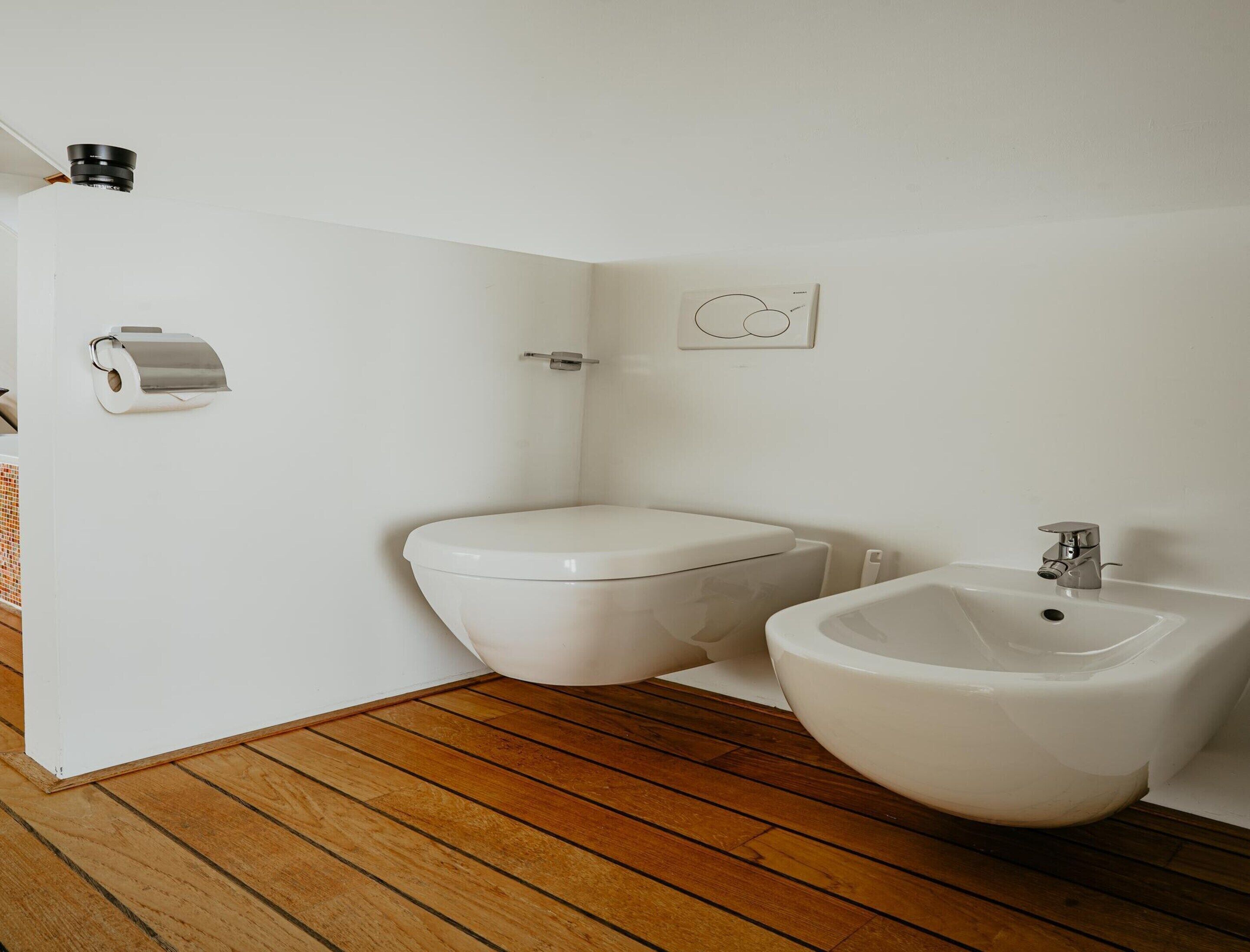 A bathroom with a toilet, bidet, and a wooden floor.