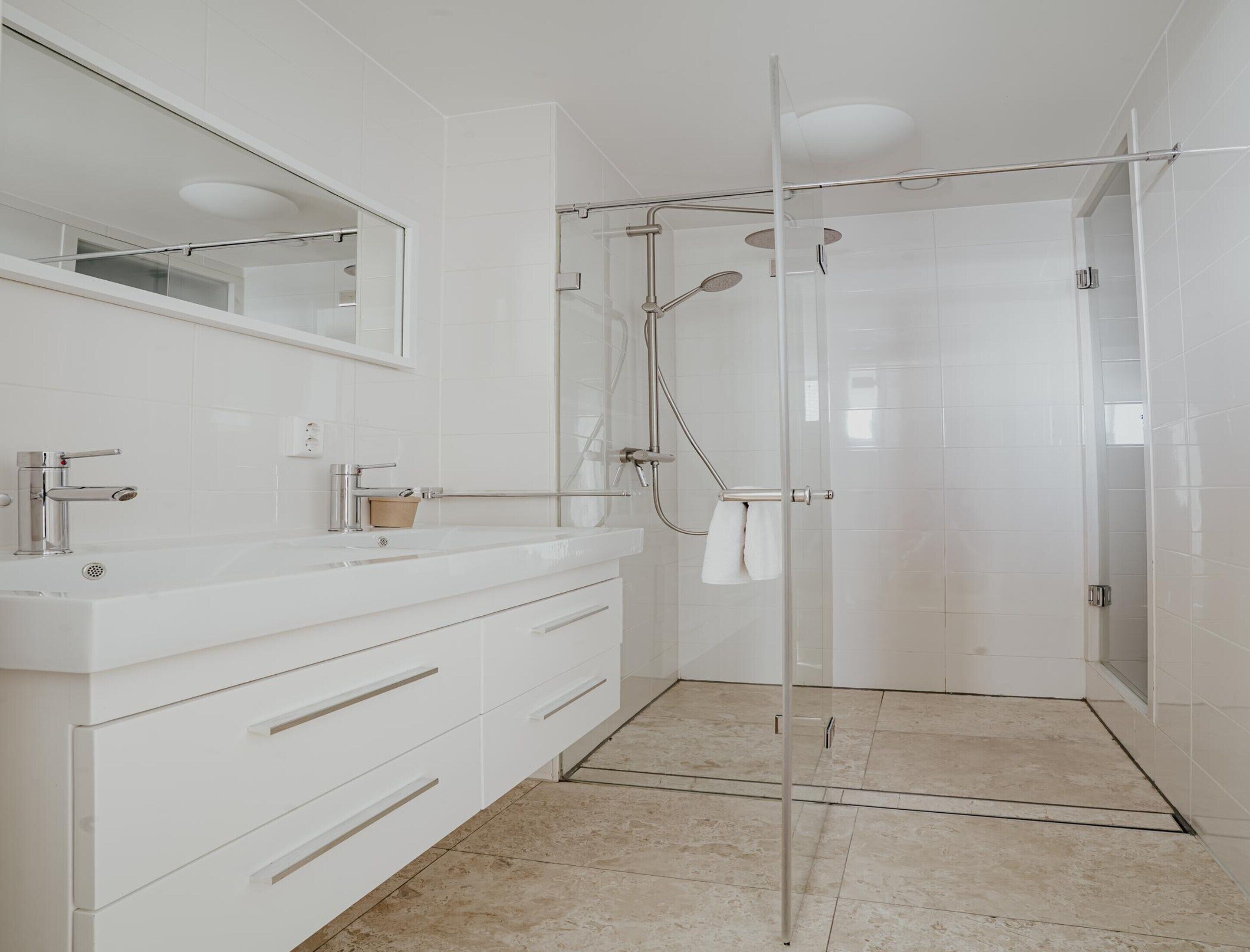 Une salle de bain moderne avec une douche à l’italienne en verre, des meubles blancs et un grand miroir.