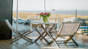 A balcony with a table and two chairs, a vase with flowers, and a view of the beach and ocean. - Apartment in Egmond With Sea Views (Egmond aan Zee)