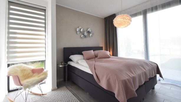 Een moderne slaapkamer met een groot bed, een zachte fauteuil en uitzicht op het groen.