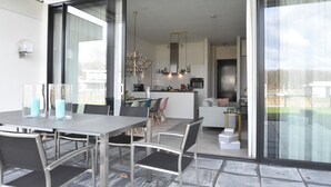 Een moderne keuken met een centraal eiland, een eethoek met tafel en stoelen, en een grote schuifpui naar een balkon.