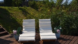 Twee witte loungestoelen op een houten terras met potplanten.