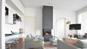 Een moderne woonkamer met een open haard, grijze banken, een salontafel en een aan de muur bevestigde televisie.