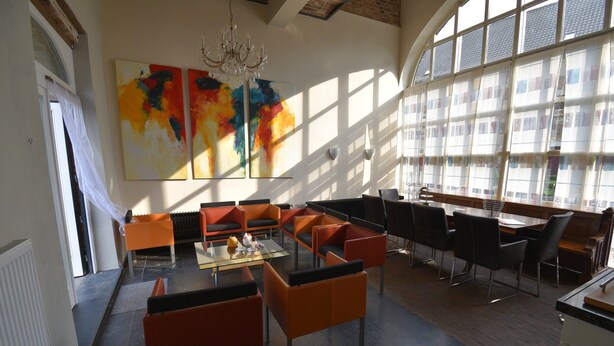 A modern dining area with orange and black chairs, a glass-top table, and abstract paintings on the wall. - Apartment Near the Belgian Border (Eijsden)
