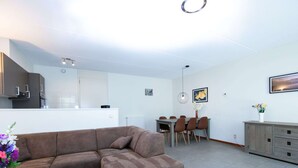 A modern living room with a brown sectional sofa, a dining table with chairs, a kitchen area, and a gray cabinet with drawers. - Cozy Forest-edge Home (Rheezerveen)