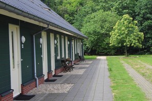 Une rangée de bâtiments verts, chacun avec une porte numérotée, des places assises à l’extérieur et un trottoir dallé.
