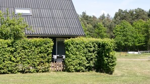 A building with a corrugated metal roof, a small window, and a door. There is a wooden fence and a hedge in front of the building. - Cozy Forest-edge Home (Rheezerveen)