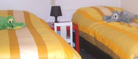 A room with two beds, each with yellow and white striped bedding. There is a lamp on a small table between the beds.