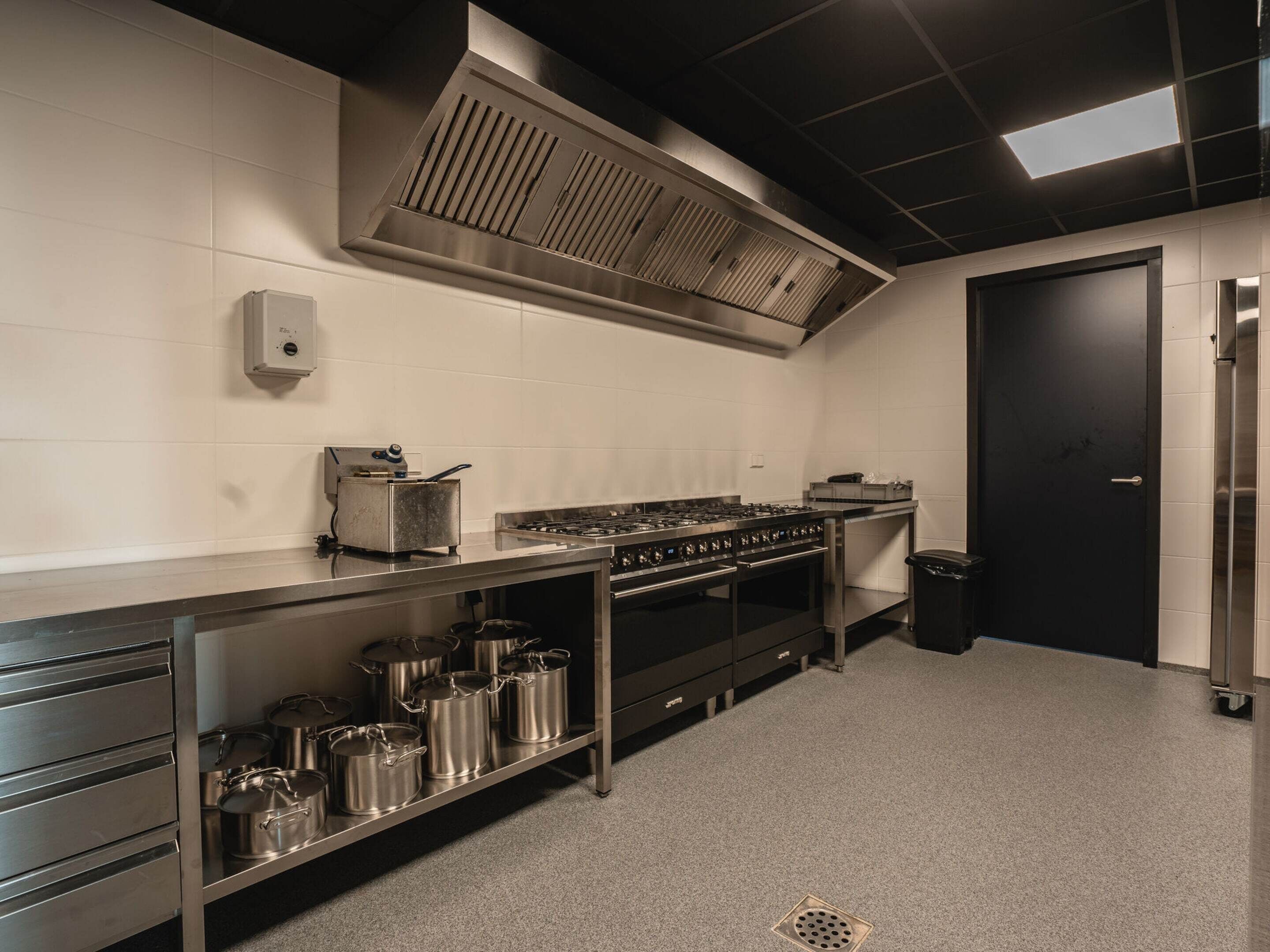 Una cocina industrial con electrodomésticos de acero inoxidable, una campana de ventilación y una puerta negra.