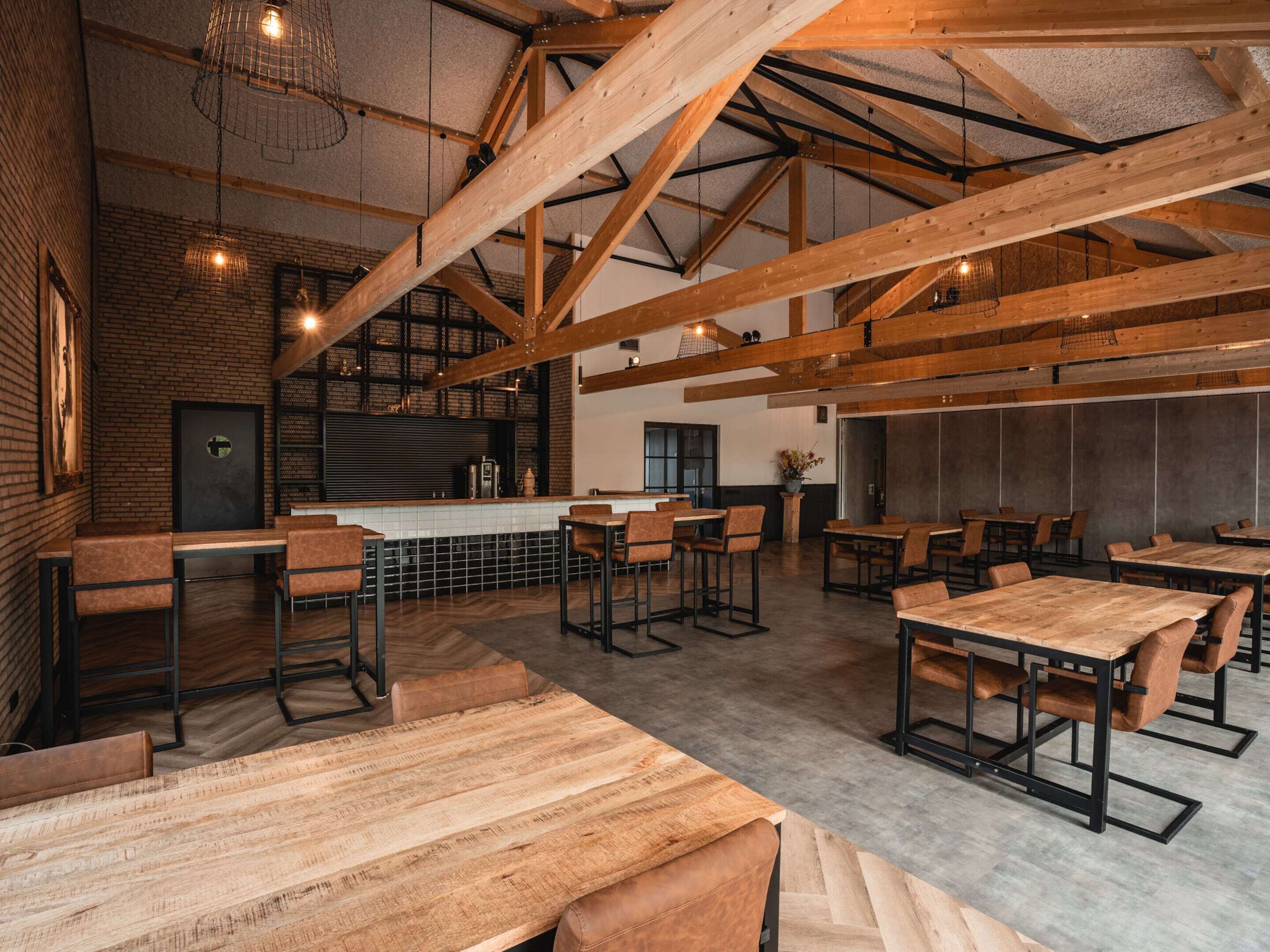 A spacious restaurant with high ceilings and exposed wooden beams, featuring a bar area and multiple seating arrangements.