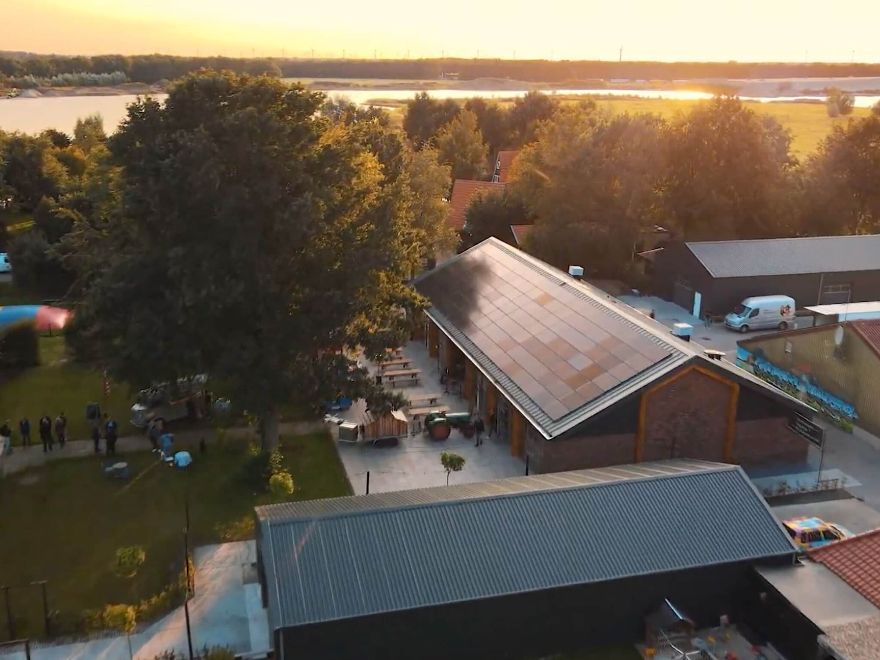 A building with a sloped roof, a covered outdoor area with tables and chairs, and a view of a lake in the background.