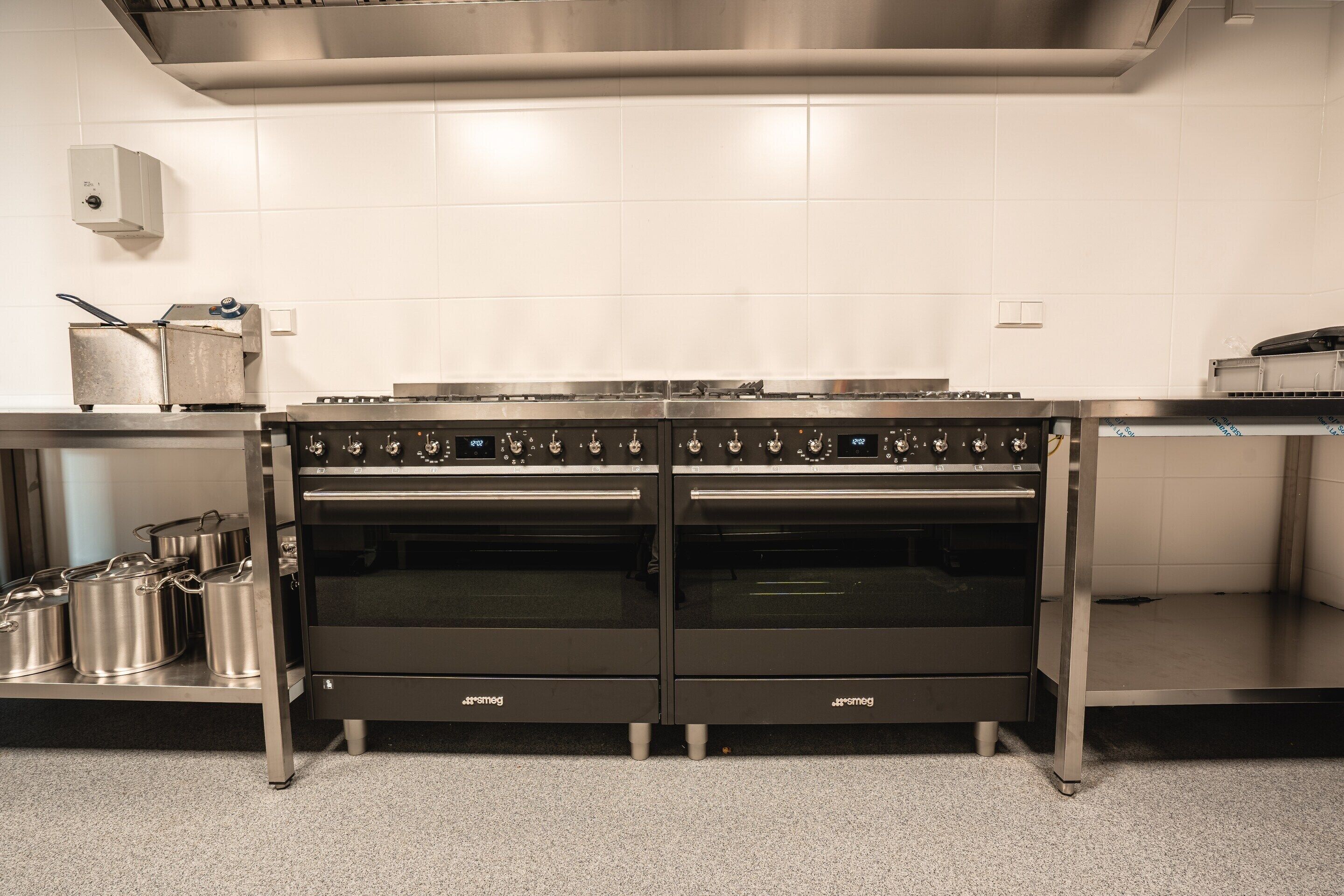 Een professionele keuken met twee roestvrijstalen ovens, een roestvrijstalen werkblad en een betegelde achterwand.