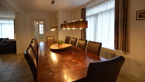 A dining area with a wooden table, chairs, a hanging light fixture, and a window with curtains.