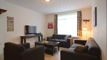Ein Wohnzimmer mit Fernseher, Sofas, Couchtisch und Lampe.