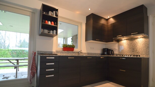A modern kitchen with dark cabinetry, a granite countertop, and a built-in stove.