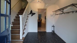 A staircase with wooden steps and white railings, a black tiled floor, a butterfly wall decoration, and a clothing rack with hangers.