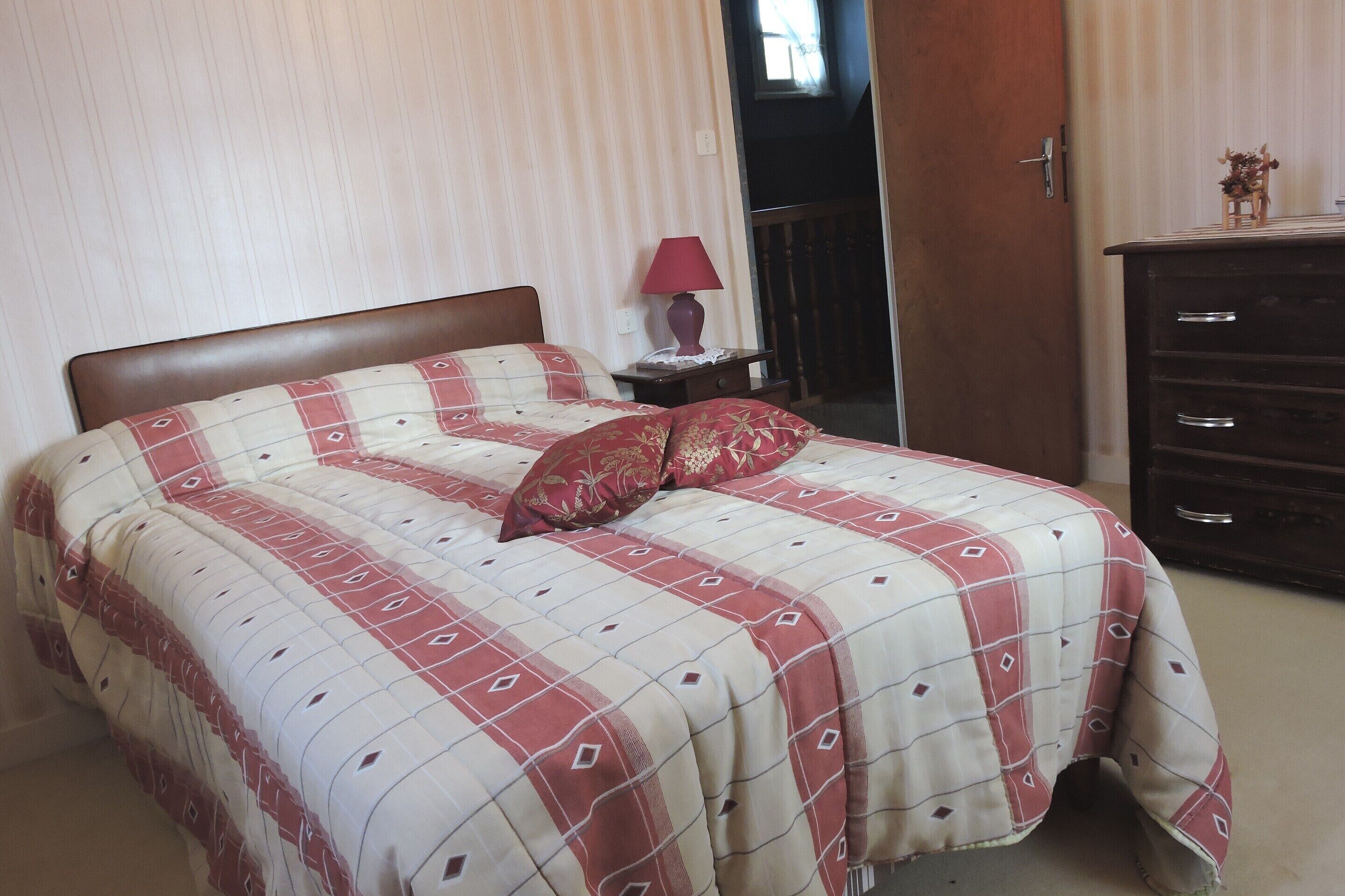 Una cama con colcha a cuadros, una mesita de noche con lámpara y un aparador con cajones.