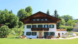 Un edificio a due piani con facciata in legno, persiane verdi e un balcone con piante in vaso.