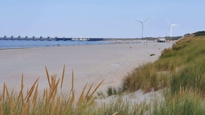 Una playa con aerogeneradores, un puente y dunas cubiertas de hierba.