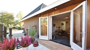 A modern house with a wooden exterior, a stone patio, and a sliding glass door leading to an interior with a fireplace and furniture. - Vintage Holiday Home in Kamperland near Lake Veerse (Kamperland)